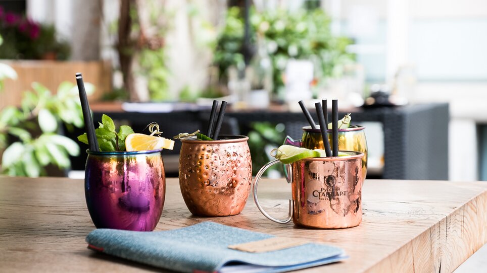 Bunte Cocktails in kupfernen Bechern auf einem Holztisch. | © Schäffner