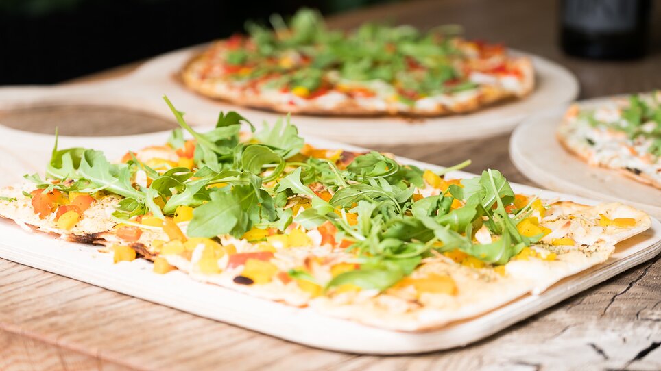 Dünne Pizza mit buntem Gemüse und Rucola auf Holzbrett. | © Schäffner