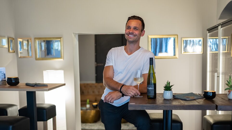 Lächelnder Mann mit Wein in einem stilvollen Raum. | © Schäffner