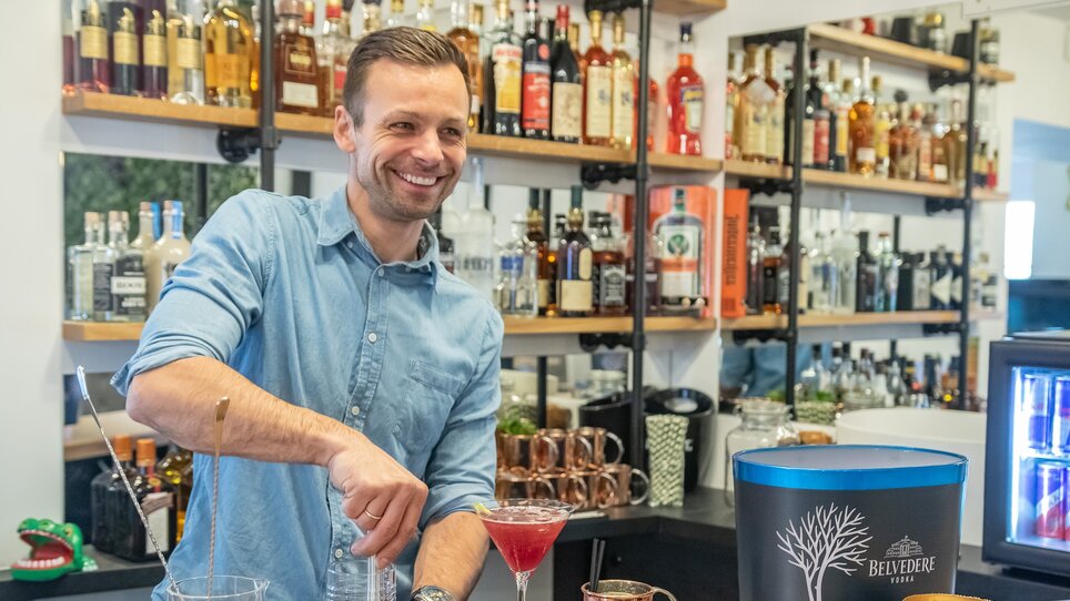 Ein Barkeeper mixt Cocktails in einer Bar mit vielen Spirituosen.