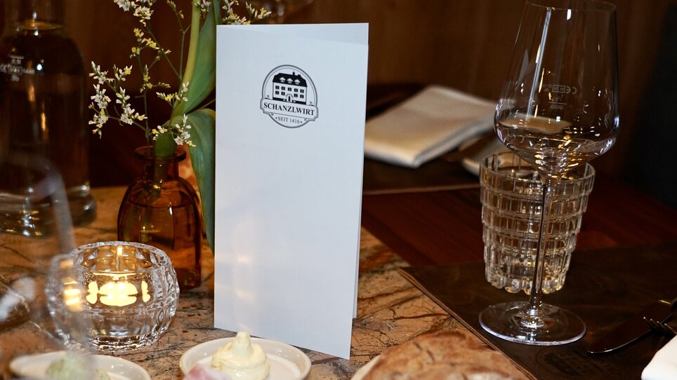 Tisch mit Menü, Brot, Aufschnitt und Blumen in einem Restaurant. | © Wirtshaus Schanzlwirt