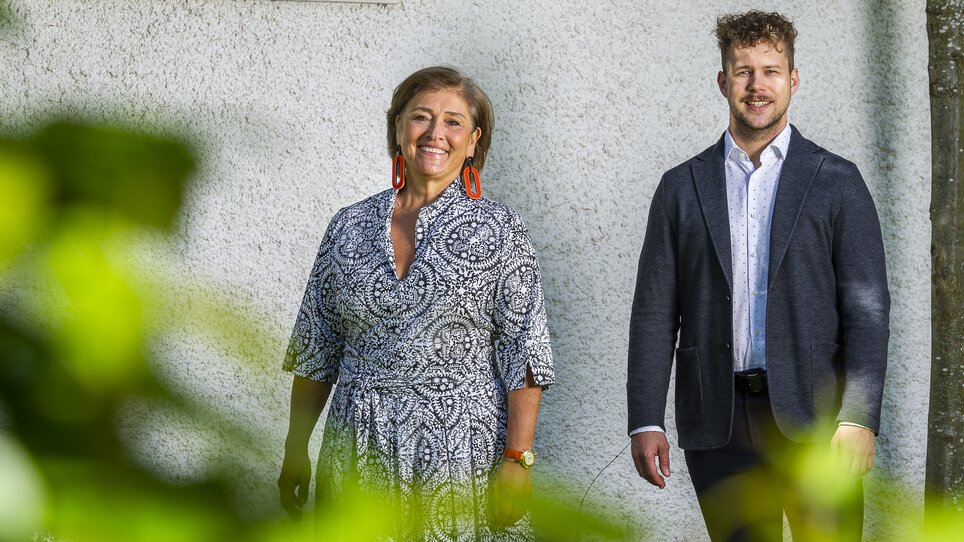 Two people stand in a garden, smiling and posing in front of a wall. | © Stammtisch am Paulustor