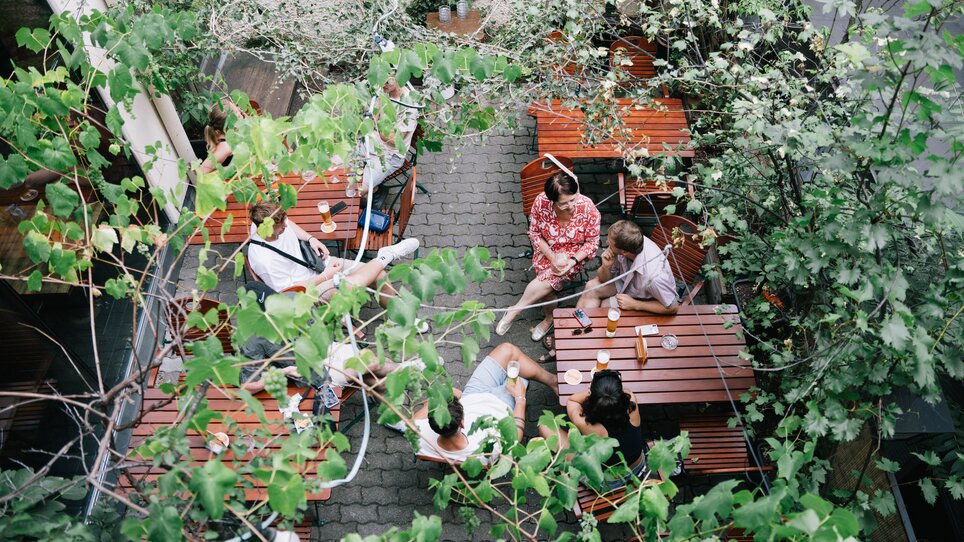 Leute entspannen in einem grünen Innenhof mit Tischen und Getränken. | © G. Obetzhofer