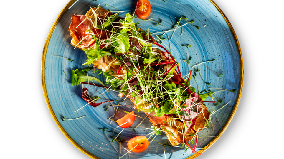 Ein elegantes Gericht mit Salat, Tomaten und frischen Kräutern auf einem blauen Teller. | © Ristorante Trenta