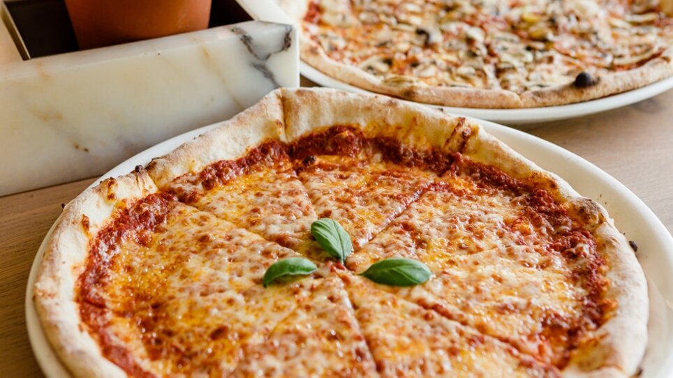 Zwei Pizzen auf einem Tisch, die eine mit Käse und Basilikum. | © VAPIANO Global