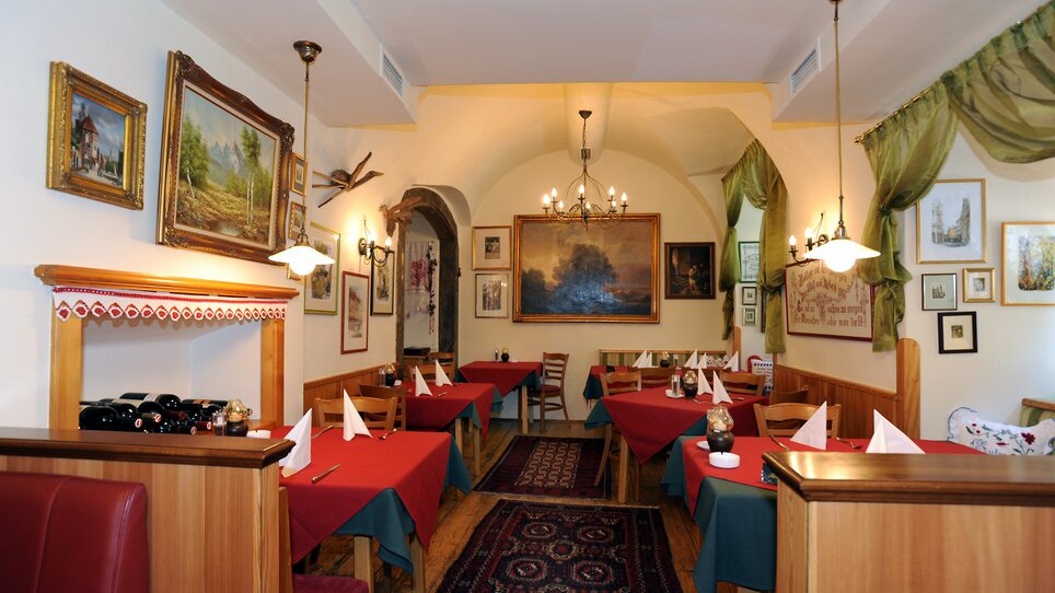 Ristorante accogliente con tavoli con tovaglie rosse e tende verdi, arte alle pareti. | © Welscher Stubn