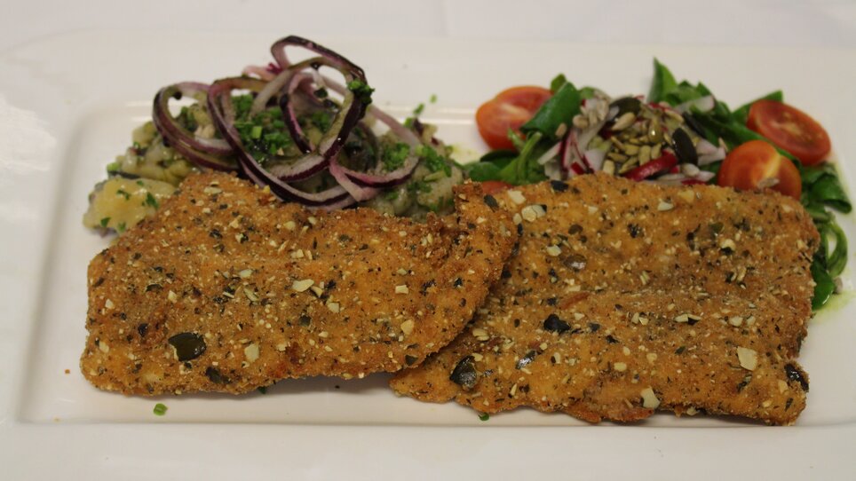 Schnitzel of turkey with pumpkin seed breading with potato salad and green salad on a square plate. | © Zur alten Press