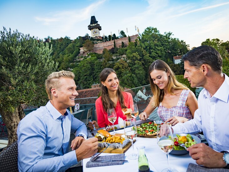 Vier Personen genießen ein Abendessen mit Blick auf den Grazer Uhrturm. | © Graz Tourismus - Werner Krug