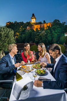 Eine elegante Dinnergruppe in Graz mit dem Grazer Uhrturm im Hintergrund. | © Graz Tourismus - Werner Krug