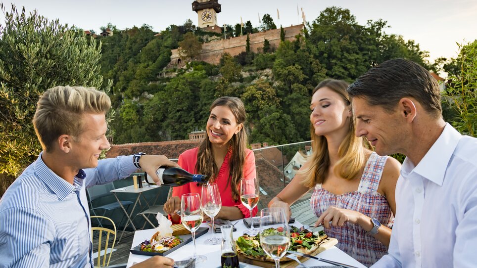 Freunde genießen ein Abendessen mit Blick auf die Grazer Uhrturm und die Stadt Graz. | © Graz Tourismus - Werner Krug