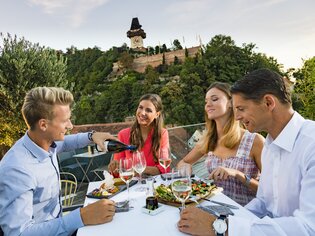 Freunde genießen ein Abendessen mit Blick auf die Grazer Uhrturm und die Stadt Graz. | © Graz Tourismus - Werner Krug