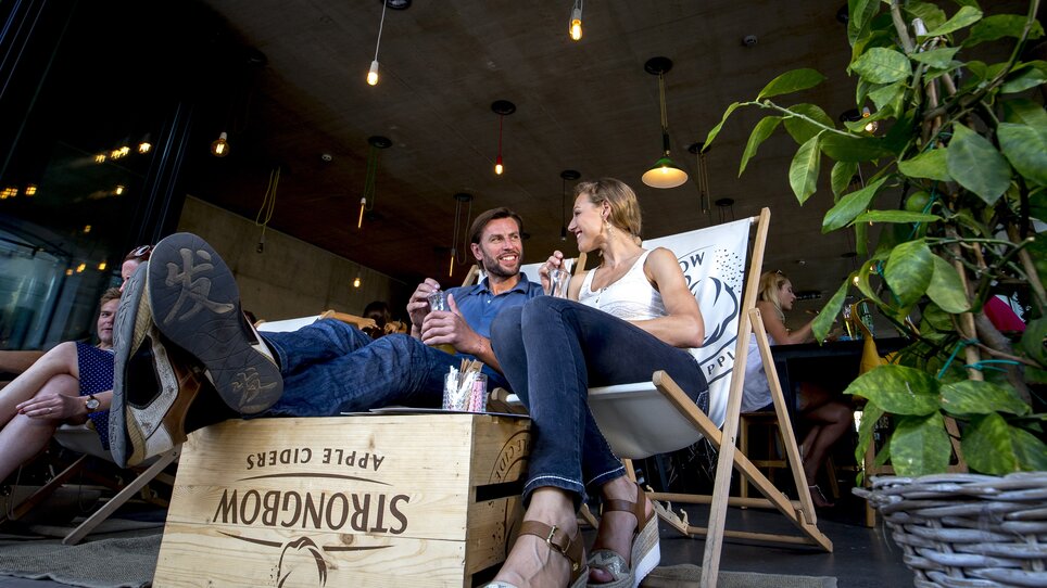 Due persone ridono e chiacchierano in un ambiente accogliente con piante e illuminazione. | © Graz Tourismus - Tom Lamm