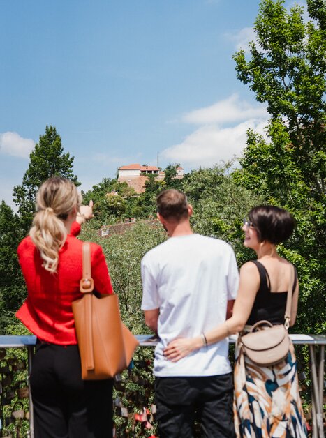 Tre persone guardano lo Schlossberg di Graz durante una visita guidata della città. | © 5komma5sinne - MotionAds