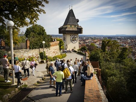 Der Grazer Uhrturm überblickt die Stadt Graz. Besucher genießen den Ausblick. | © Graz Tourismus - Werner Krug