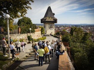 Der Grazer Uhrturm überblickt die Stadt Graz. Besucher genießen den Ausblick. | © Graz Tourismus - Werner Krug