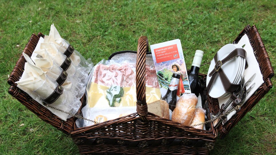 Ein Picknickkorb voller Leckereien, Wein und Brote auf grünem Rasen. | © Graz Tourismus -  Harry Schiffer