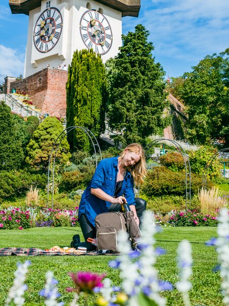 Young woman having a picnic in the green with Graz's Clock Tower in the background. | © Mias Photoart