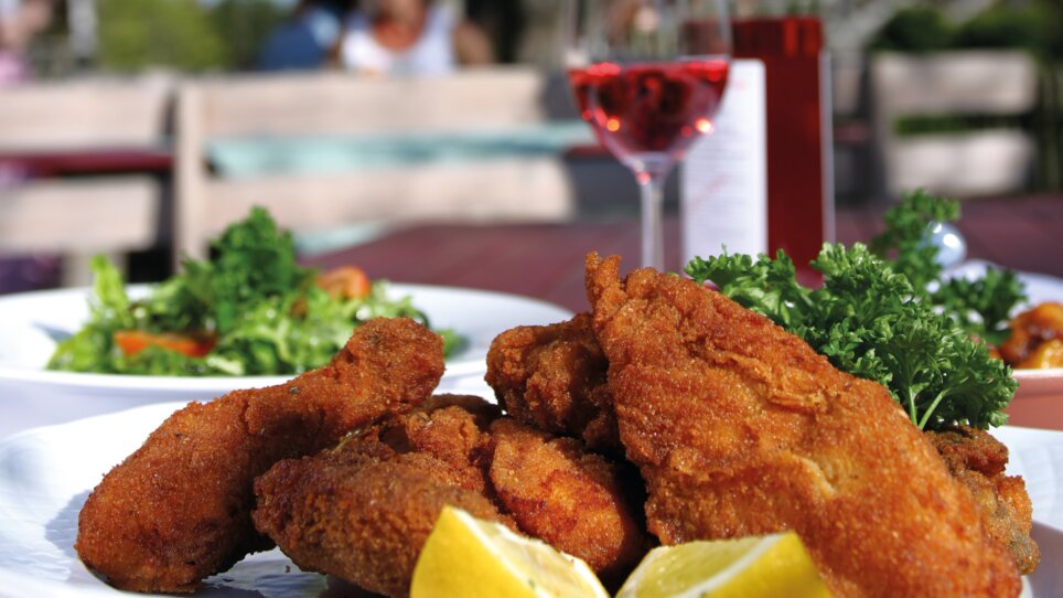 Pollo impanato con limone su un piatto davanti a un albero in fiore. | © Graz Tourismus - Harry Schiffer
