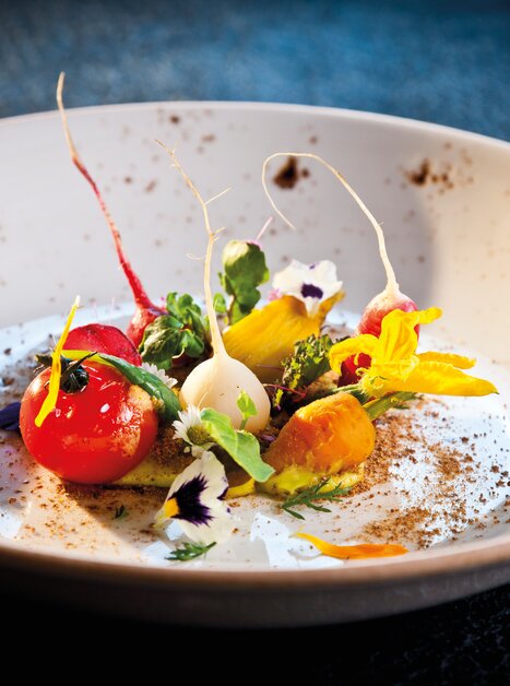 An artistically arranged gourmet dish featuring colorful ingredients and flowers. | © Graz Tourismus - Werner Krug