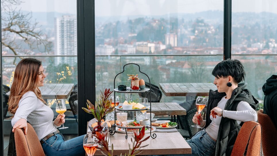 Due donne che gustano brunch e cocktail a aiola upstairs con vista su Graz. | © 5komma5sinne - Rene Strasser Fotografie 