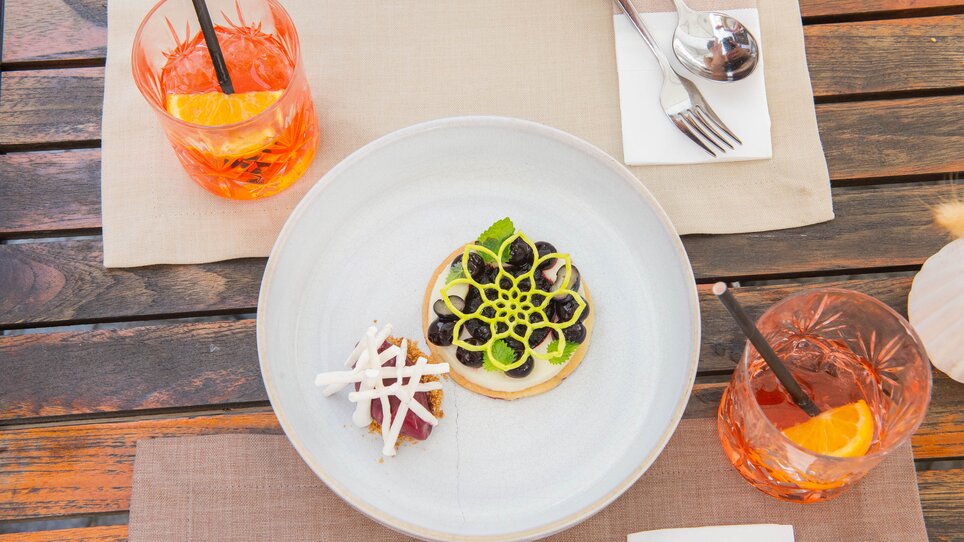 Ein elegantes Gericht mit zwei kleinen Speisen auf einem Teller, serviert mit Getränken. | © 5komma5sinne - Helmut Schweighofer