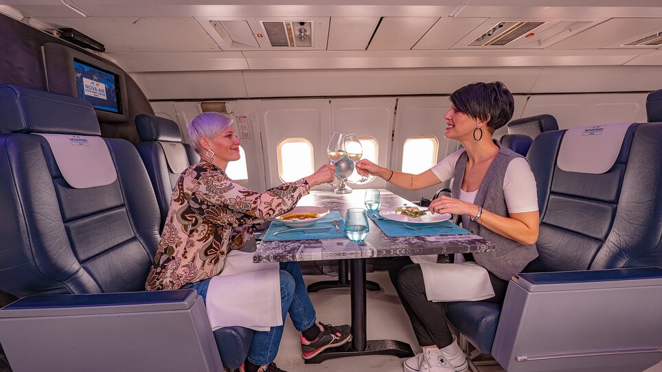 Zwei Frauen stoßen in einem Flugzeug im NOVA-AIR in Graz mit Gläsern an. | © 5komma5sinne - Rene Strasser Fotografie