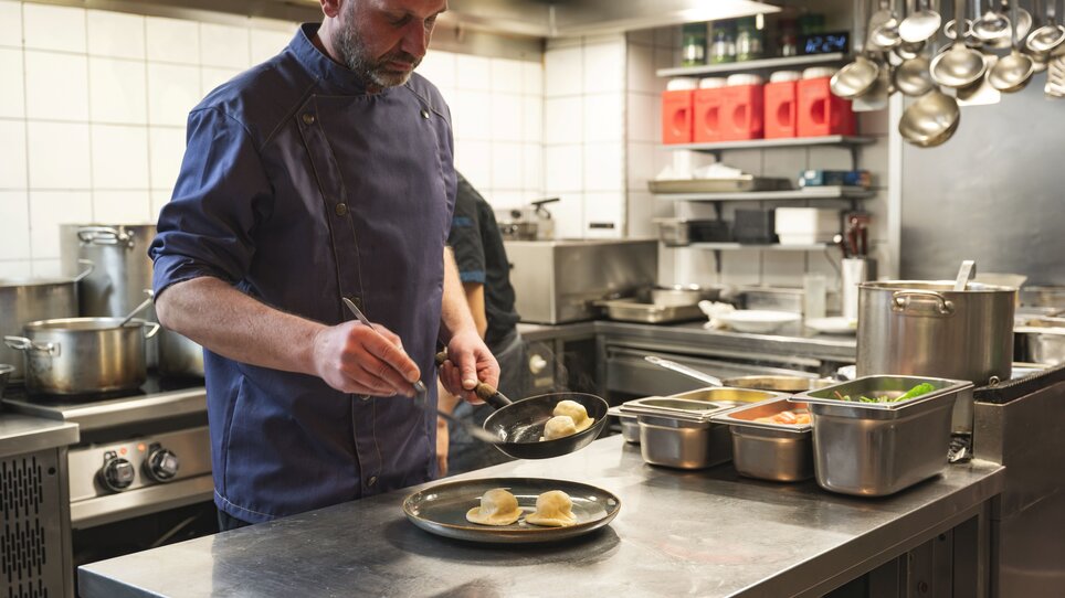 Uno chef del ristorante “Zur Steirerstub'n” di Graz prepara un piatto su una piastra in cucina. | © 5komma5sinne - Rene Strasser Fotografie 
