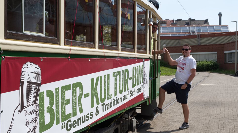 A man poses next to the beer culture tram with a large banner. | © Tramway Museum Graz