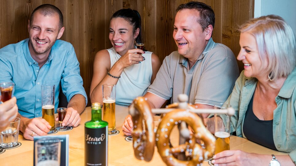 Four people are having fun at a social gathering with beer and pretzels. | © Mias Photoart