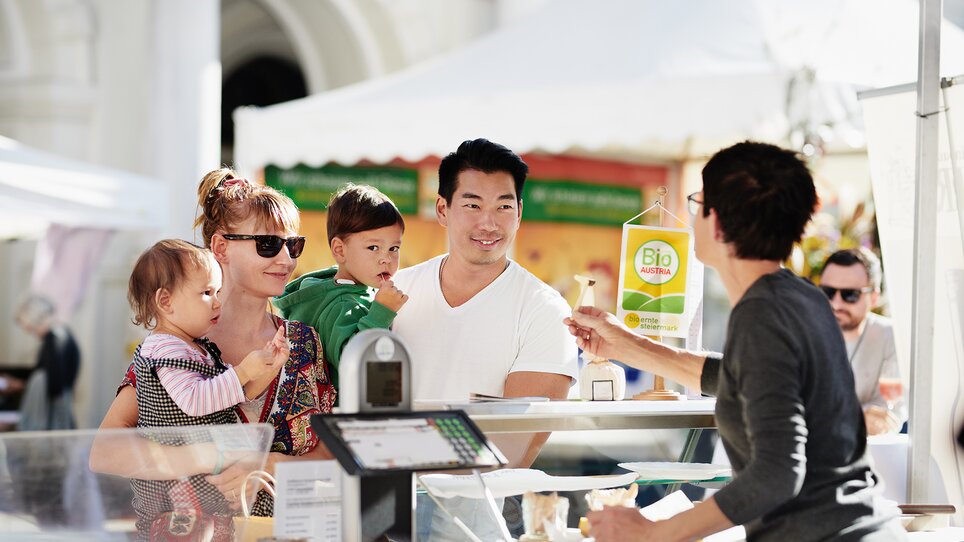 Eine Familie mit zwei Kleinkindern an einem Marktstand. | © BIO AUSTRIA Steiermark - Königshofer