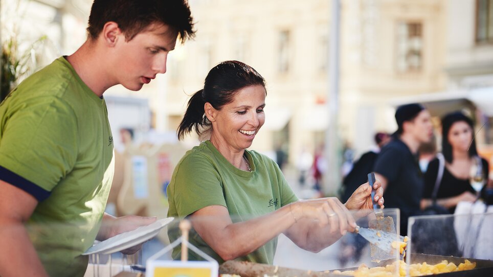 Zwei Personen in grünen Kleidern bereiten Streetfood an einem Verkaufsstand zu. | © BIO AUSTRIA Steiermark - Königshofer
