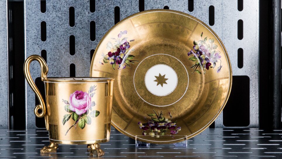Ein goldener Becher und Untertasse mit Blumenmotiven auf einem Regal. | © Markus Mansi_MOMA