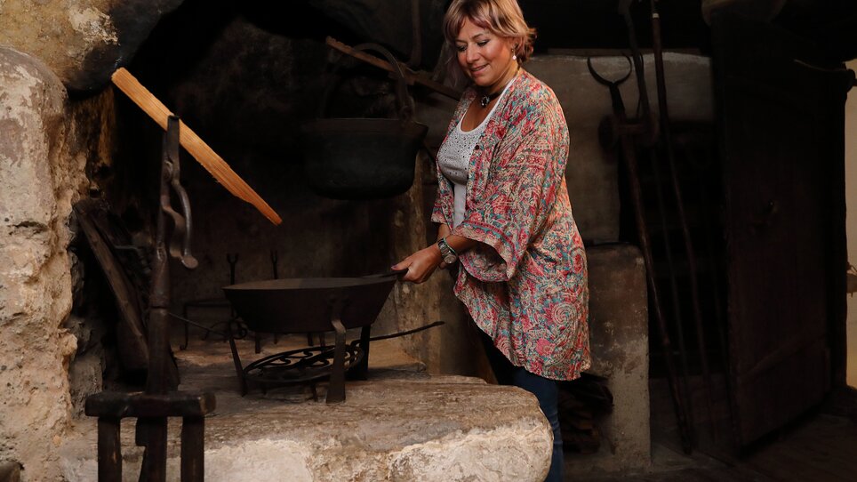 Frau steht an einem historischen Herd im Volkskundemuseum. | © Universalmuseum Joanneum - J. J. Kucek