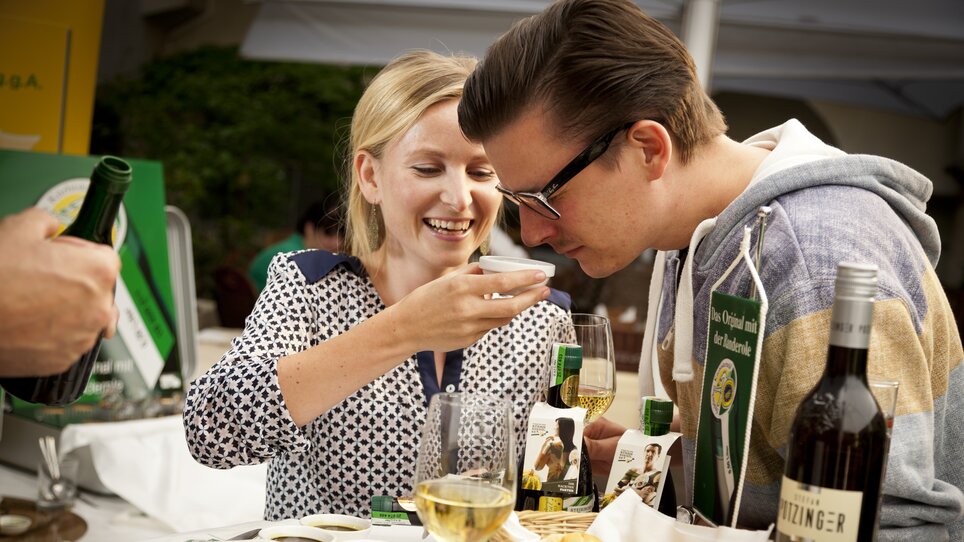 Zwei Personen probieren Kürbiskernöl in Graz, umgeben von Wein und Snacks. | © Graz Tourismus - Werner Krug