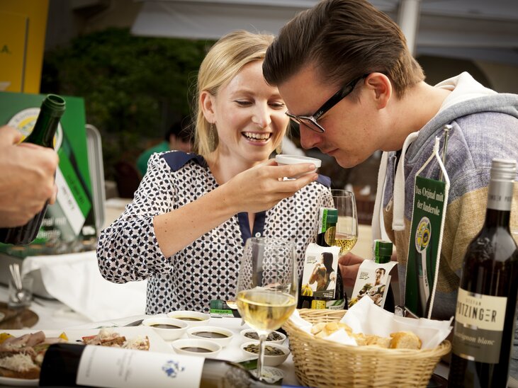 Zwei Personen probieren Kürbiskernöl in Graz, umgeben von Wein und Snacks. | © Graz Tourismus - Werner Krug