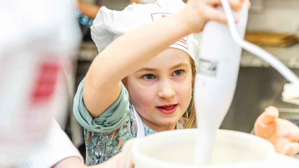 Ein Mädchen bedient einen Handmixer bei einem Kinder-Kochkurs. | © Graz Tourismus - Paul Stajan