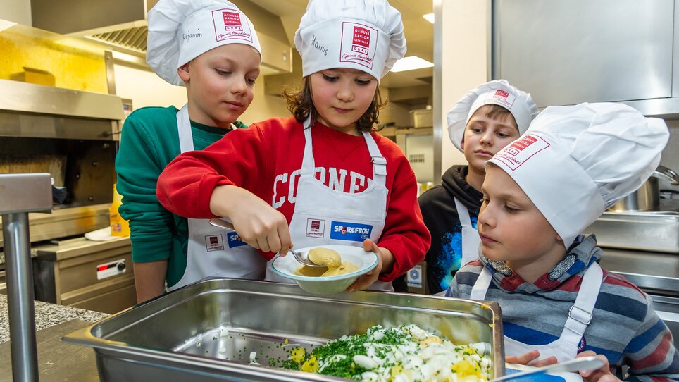 Vier Kinder in Kochmützen bereiten gemeinsam ein Gericht vor. | © Graz Tourismus - Paul Stajan