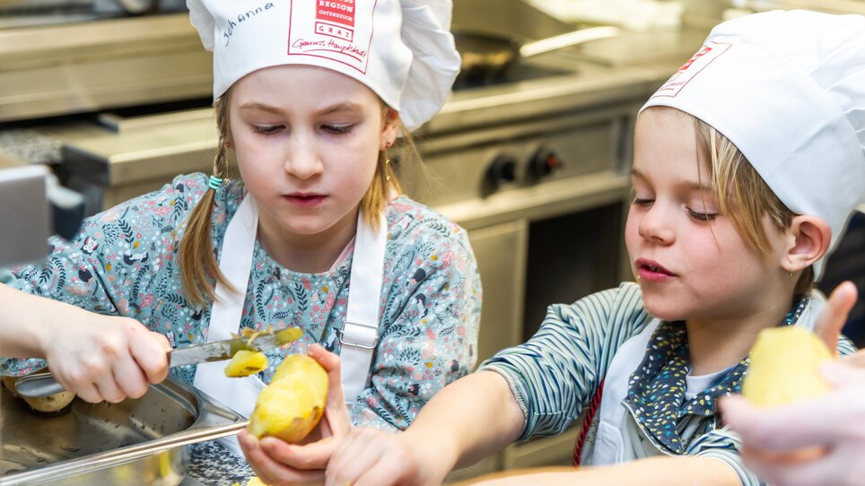 Zwei Kinder schälen Kartoffeln in einer Küche bei einem Kochkurs. | © Graz Tourismus - Paul Stajan