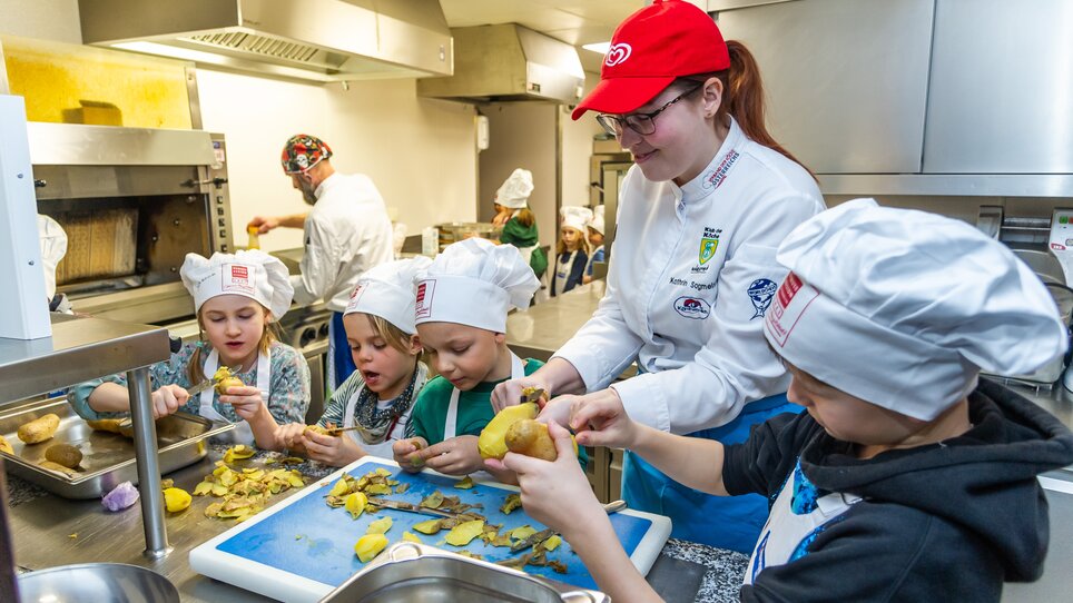 Kinder lernen beim Kochkurs, unter Anleitung einer Köchin, Kartoffeln zu schälen. | © Graz Tourismus - Paul Stajan