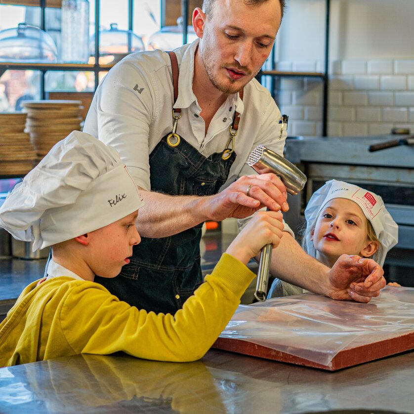 Kinderkochkurs in der GenussHauptstadt Graz | © Milena Bonstingl Ein Koch in einer Küche zeigt Kindern bei einem Kochkurs, wie man Teig zubereitet. | © Milena Bonstingl