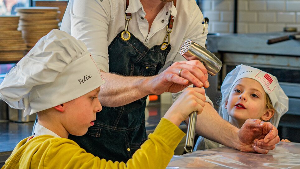 Ein Koch in einer Küche zeigt Kindern bei einem Kochkurs, wie man Teig zubereitet. | © Milena Bonstingl
