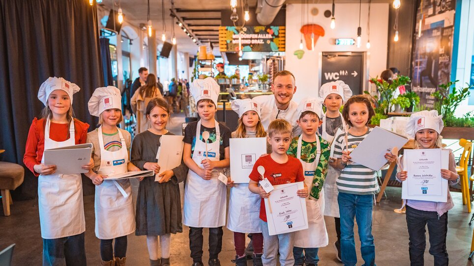 Kinder und ein Koch posieren nach dem Kochkurs mit Urkunden. | © KHC - Bernhard Schindler