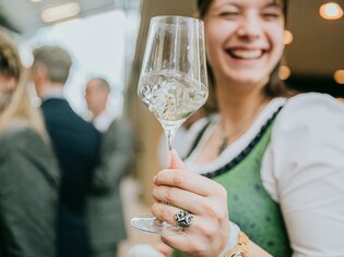 Lächelnde Frau hält ein Weinglas, während sie in einer festlichen Umgebung ist. | © Wein Steiermark - Johanna Lamprecht