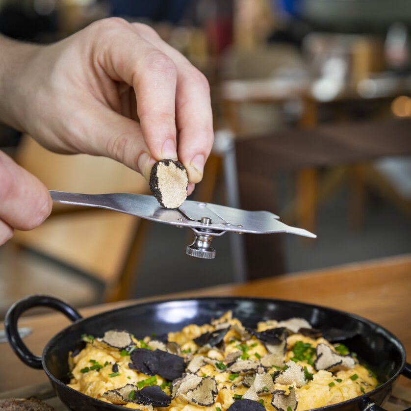 A hand holding a truffle slicer over a dish of eggs and truffles. | © Graz Tourismus - Werner Krug