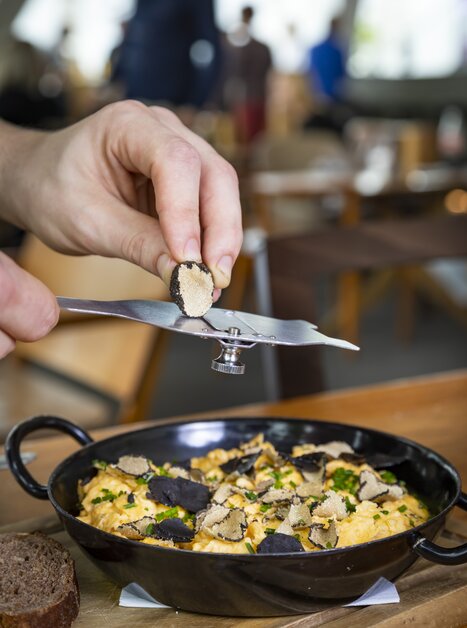 A hand holding a truffle slicer over a dish of eggs and truffles. | © Graz Tourismus - Werner Krug