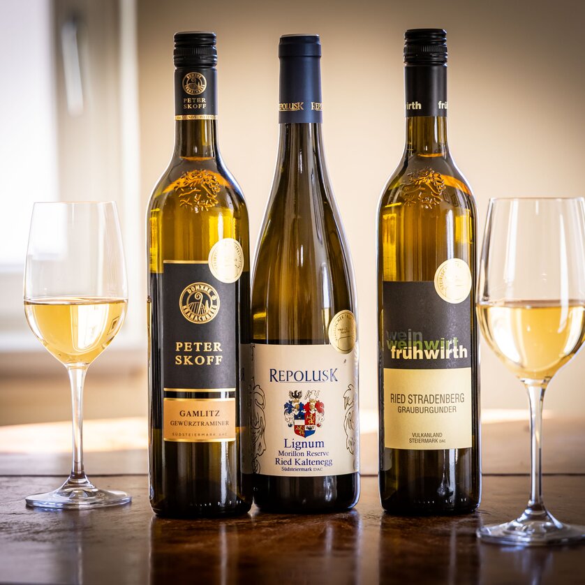 Drei Flaschen Weißwein stehen zwischen zwei Weingläsern auf einem Tisch. | © Graz Tourismus - Werner-Krug