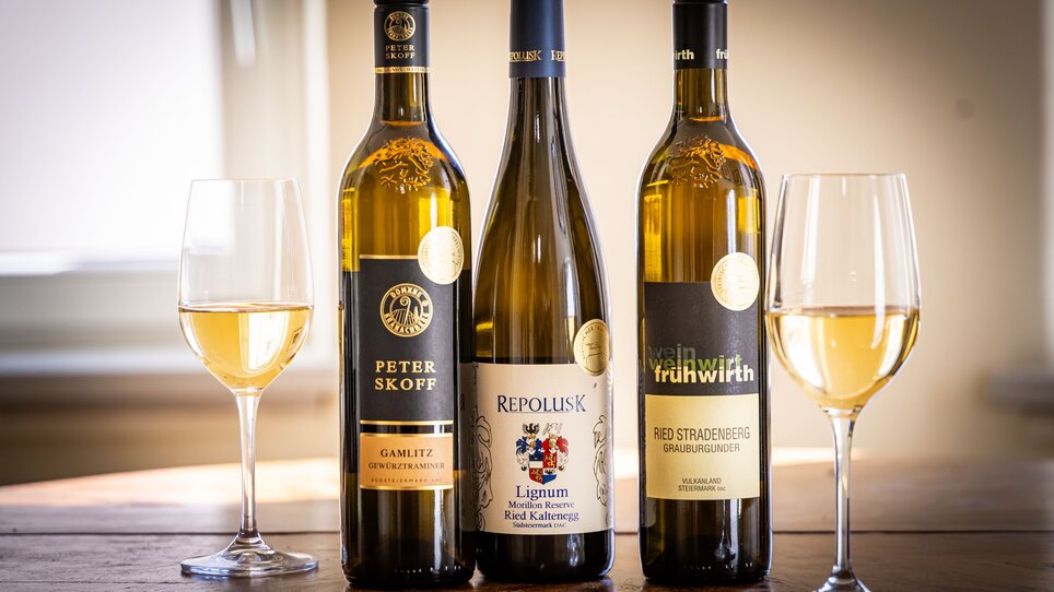 Three bottles of white wine are standing on a table between two wine glasses. | © Graz Tourismus - Werner-Krug