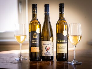 Drei Flaschen Weißwein stehen zwischen zwei Weingläsern auf einem Tisch. | © Graz Tourismus - Werner-Krug