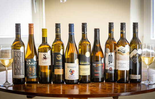 Eine Auswahl an Weißweinflaschen auf einem Holztisch, mit zwei Gläsern Wein. | © Graz Tourismus - Werner Krug