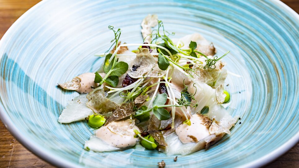 Un'insalata di tartufo elegantemente presentata con varie erbe e una salsa cremosa su un piatto decorativo. | © Graz Tourismus - Werner Krug